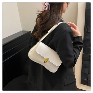 Close-up of a white leather underarm bag with an oval gold metal lock on a black blazer