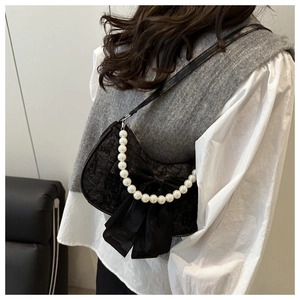 Detail showing a black lace handbag with a silk bow and elegant pearl beaded handle