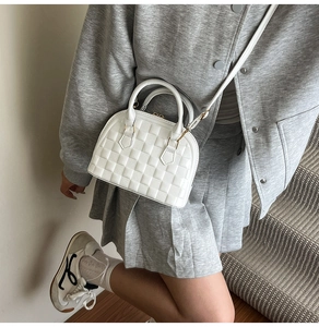 Close-up of white shell-shaped handbag with quilted pattern worn by a model on stairs