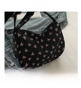 Close-up of black pleated underarm bag featuring pink bow pattern on denim jacket