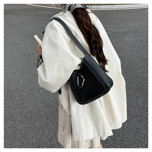 Gros plan du sac seau noir avec boucle dorée organique et surpiqûres blanches contrastées