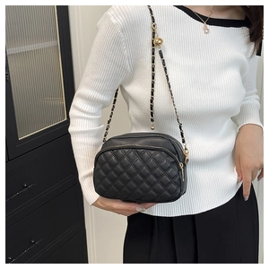 Close-up of black quilted leather crossbody bag with golden chain and decorative ball