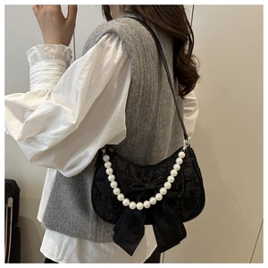 Detail of black lace shoulder bag with a large bow and decorative pearl chain strap