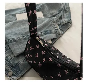 Detail of black quilted shoulder bag with pink bow pattern and smooth metal zipper