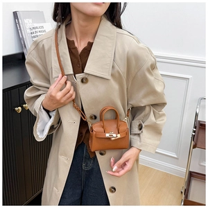 Miniature caramel brown leather handbag with gold metal lock worn over a trench coat