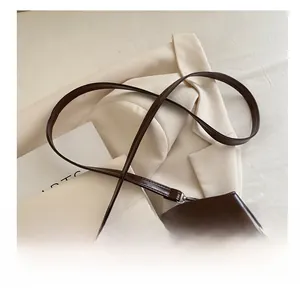 Detail view of smooth brown oil-wax leather shoulder bag straps on a beige blazer