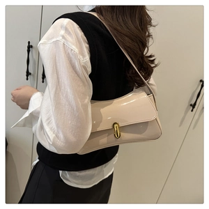 Detailed view of glossy cream patent leather baguette bag with gold oval metal buckle