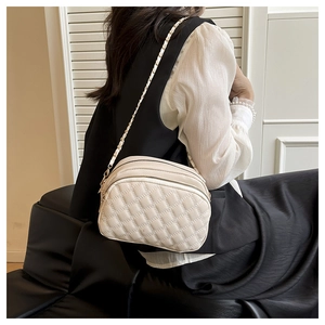 Detail view of cream quilted crossbody bag with three zipper compartments and gold chain