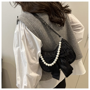 Detail of black crescent shoulder bag featuring large satin bow and pearl chain strap