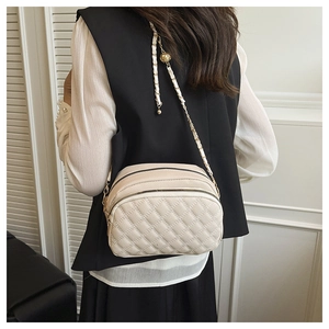 Quilted beige crossbody bag with chain strap and three zippers shown on a person