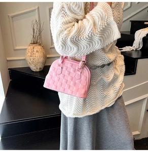 Pink embossed shell handbag with woven pattern held by a model on stairs