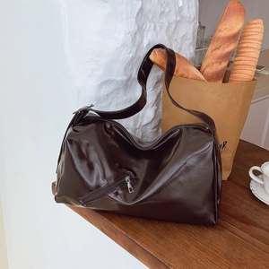 Large dark brown leather tote bag with glossy finish and decorative zipper on a wooden table