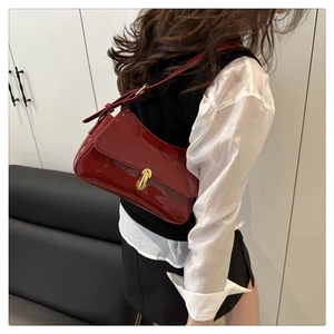 Detail of burgundy patent leather underarm bag with a glossy finish and gold metal clasp