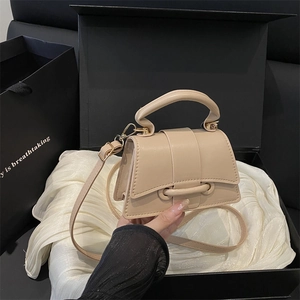Sac à main trapèze beige minimaliste avec garniture dorée posé sur boîte cadeau