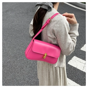 Outdoor shot of a magenta shoulder bag with gold metal clasp and smooth leather texture