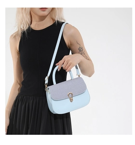 Close-up of light blue flap bag featuring striped fabric panel and gold water-drop lock