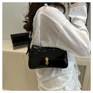 Detail of black patent leather baguette bag with a polished oval gold buckle lock