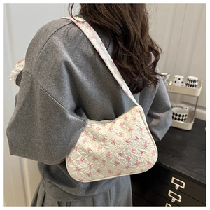 Detail of white quilted underarm bag featuring pink bow pattern and textured fabric