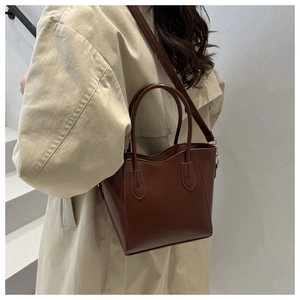 Détail du sac seau en cuir marron foncé montrant le logo gaufré et la texture de la bandoulière