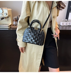 Detail of black glossy shell bag with woven texture carried by model in cafe