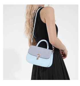 Detalle de bolso bandolera azul claro con textura tejida gris y cierre metálico