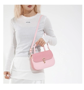 Detail shot of pink saddle bag featuring woven texture and gold metal clasp on a white outfit