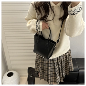 Détail du sac seau minimaliste en cuir PU noir porté avec une tenue de style preppy