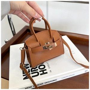 Detail of brown lychee grain leather mini handbag with gold rotating lock on a book