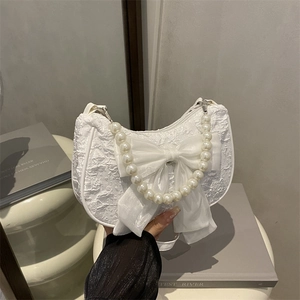 White pleated half-moon handbag with large bow and pearl handle in a stylish setup