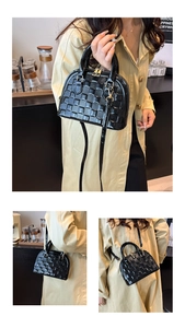 Detail of black glossy shell bag with woven texture, dual handles and golden hardware