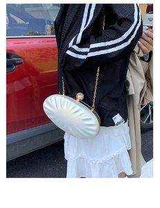 Detailed view of a white ruched shell bag with a pearl clasp and gold chain strap