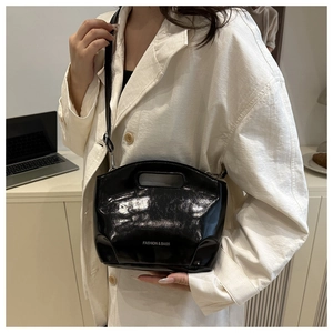 Detail of glossy black patent leather bucket bag with top handle and brand lettering