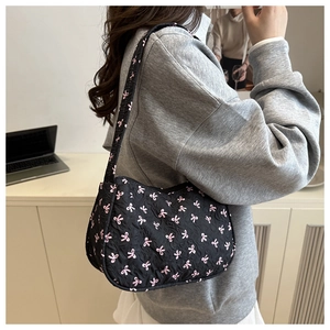 Detail view of black quilted baguette bag featuring pink bow pattern on shoulder