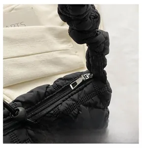 Detail of black quilted puffer shoulder bag with silver zipper and ruffled strap design