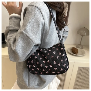 Detail of black pleated fabric underarm bag with pink bow patterns on a model