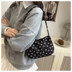 Detail of black underarm bag with pink bow pattern and quilted texture on shoulder