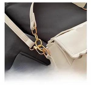 Detail of white leather shoulder bag featuring wavy edges and polished gold metal buckle
