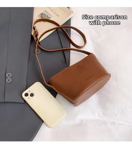 Detail view of brown lychee leather crossbody bag next to a phone for size reference