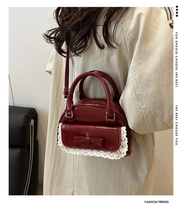 Detail of burgundy retro handbag with white lace trim and bow on cream coat outfit