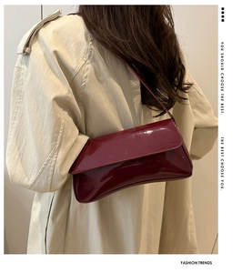 Detail of glossy deep wine red patent leather shoulder bag with smooth flap and slim strap