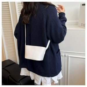 Close-up of a white lychee grain leather crossbody bucket bag with FASHION text detail