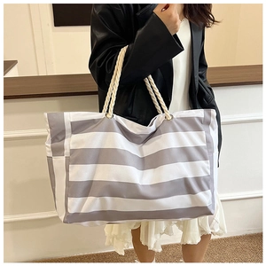 Detail of grey striped canvas tote bag with thick rope handles shown on shoulder