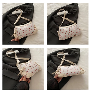 Detail view of cream shoulder bag with red cherry prints and side bow decoration