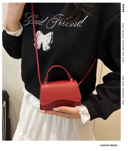 Detail of red crocodile embossed mini handbag with top handle and leather shoulder strap