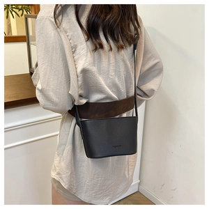 Detail of black lychee grain leather crossbody bag with embossed fashion logo and strap