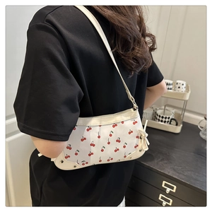 Detail of cream shoulder bag with red cherry prints and side bow tassel accent