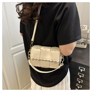 Detail of woven cream crossbody bag showing wavy trim and golden chain strap