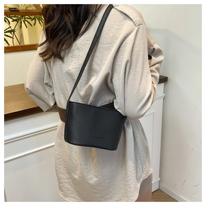 Crossbody view of black litchi texture leather bucket bag worn by model on shoulder