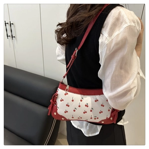 Shoulder bag featuring red cherry print and decorative bow detail on white base