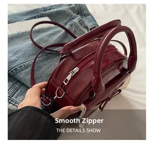 Close-up of smooth zipper and lace bow detail on burgundy patent leather bowling bag